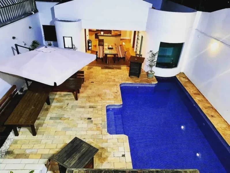 Piscina iluminada com deck, mesa e guarda-sol em uma das casas